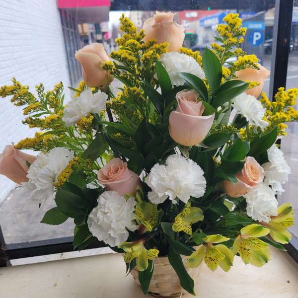 Basket arrangement of pale pink roses, white carnations, and yellow filler flowers