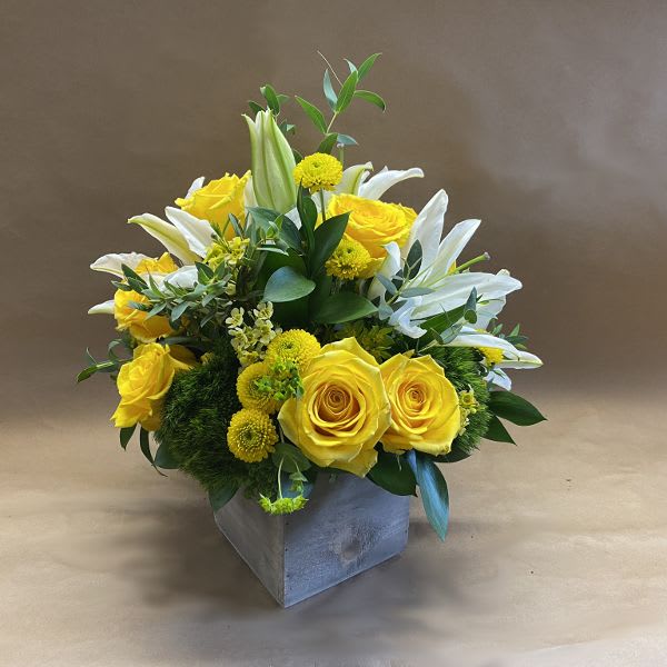 Yellow roses and white lilies arranged in a square vase