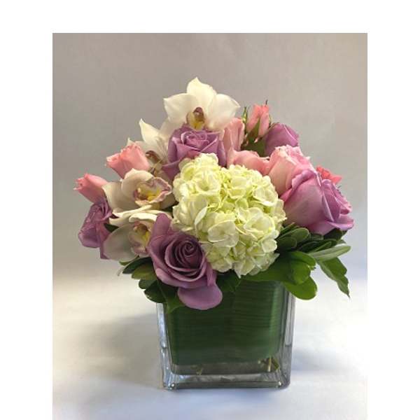Pink and lavender flowers arranged in a square glass vase