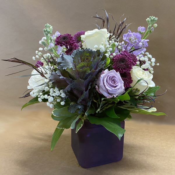Purple and white floral arrangement in a dark square vase