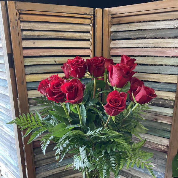 Red roses in a clear glass vase with fern foliage