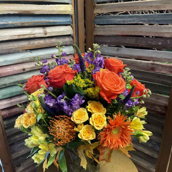 Colorful mixed bouquet with roses, purple blooms, and orange gerbera daisies in a vase