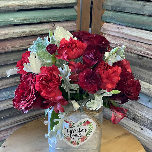 Red floral arrangement in a metal container with a heart label
