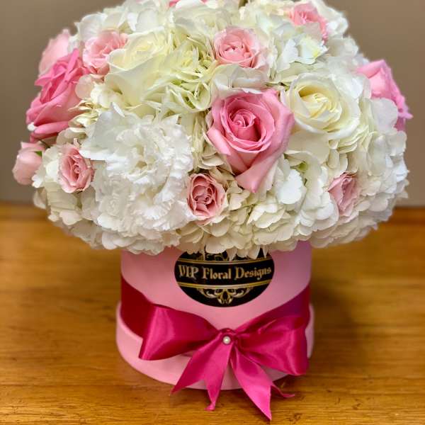 Pink and white roses arranged in a round hat box with a satin bow