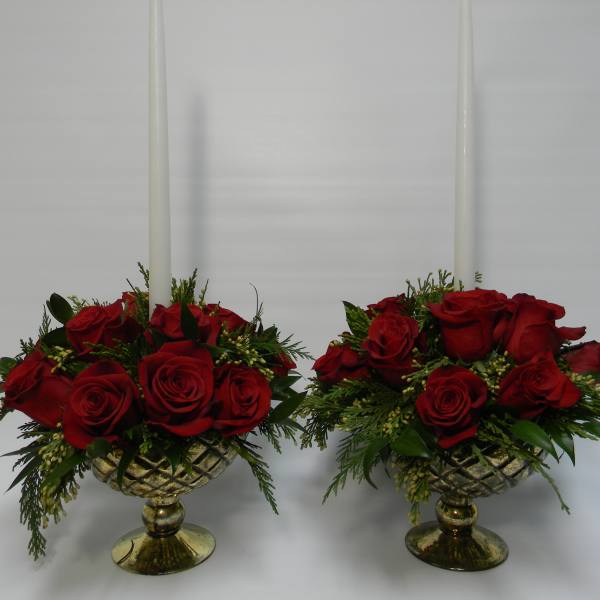 Two red rose arrangements in gold pedestal bowls with tall white candles