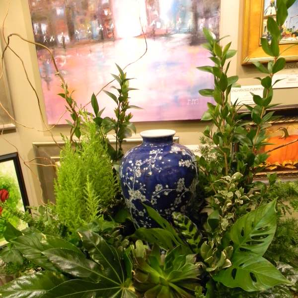 Lush green plant arrangement around a blue ceramic vase