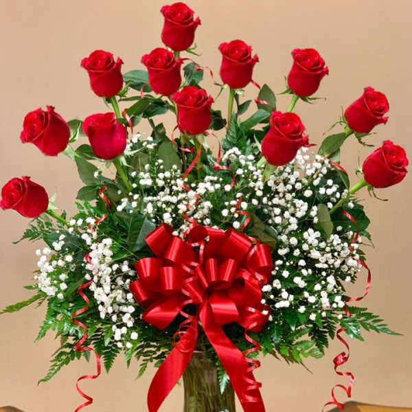 Red roses in a clear glass vase with baby's breath and a red bow
