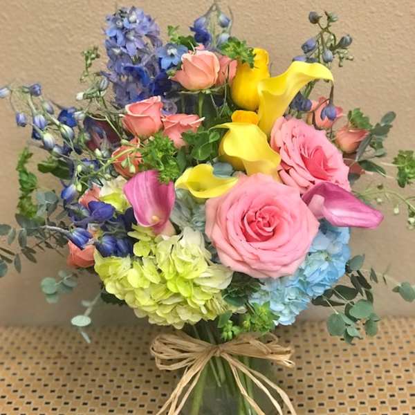 Mixed bouquet with pink roses, yellow calla lilies, and blue flowers in a glass vase