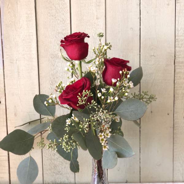 Three red roses in a clear glass vase with white filler flowers