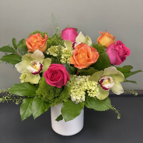 Pink and orange roses with orchids in a white vase