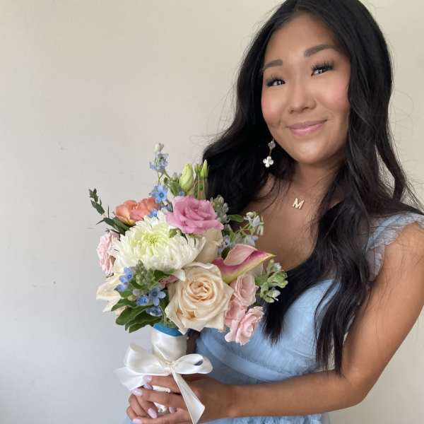 Woman holding a pastel bouquet with roses, calla lily, and white ribbon