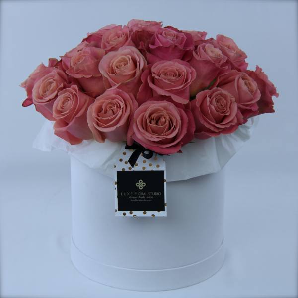 Pink roses arranged in a white hat box with a hanging tag