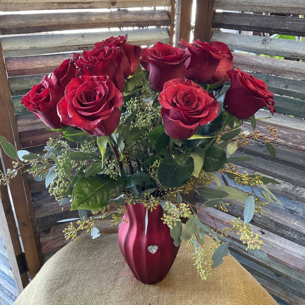 Red roses arranged in a red vase on a burlap-covered table