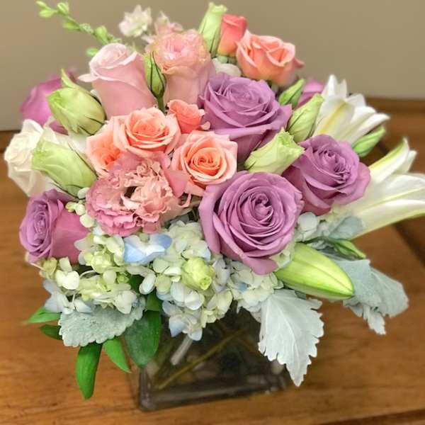 Bouquet of pink, lavender, and peach roses with lilies in a glass vase