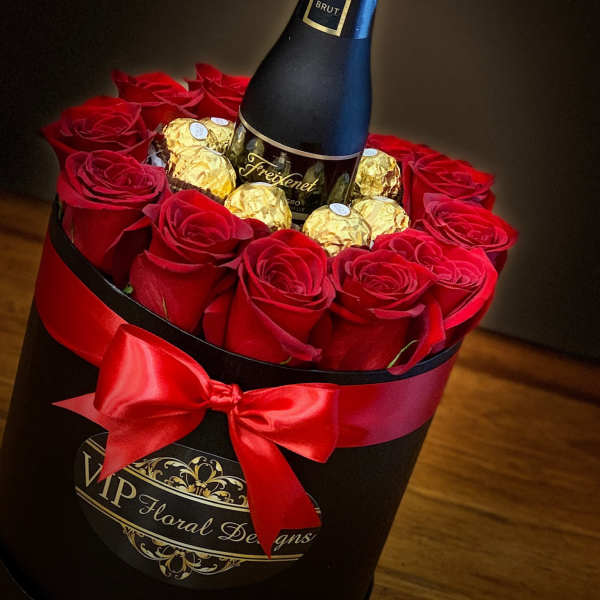 Red roses and gold chocolates arranged around a champagne bottle in a black box
