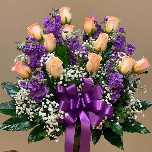 Bouquet of peach roses and purple flowers in a glass vase with a purple ribbon