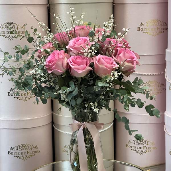 Pink roses in a clear glass vase with eucalyptus and a pink ribbon