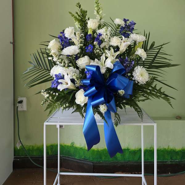 Large white and blue floral spray with a ribbon bow on a stand