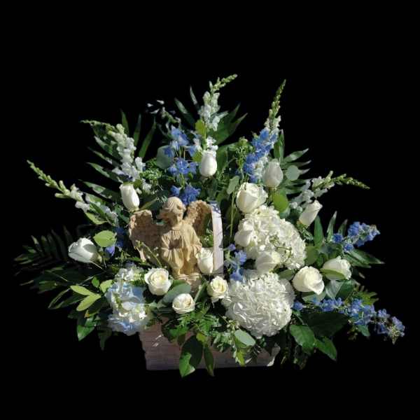 White roses and blue flowers arranged with an angel figurine in a basket