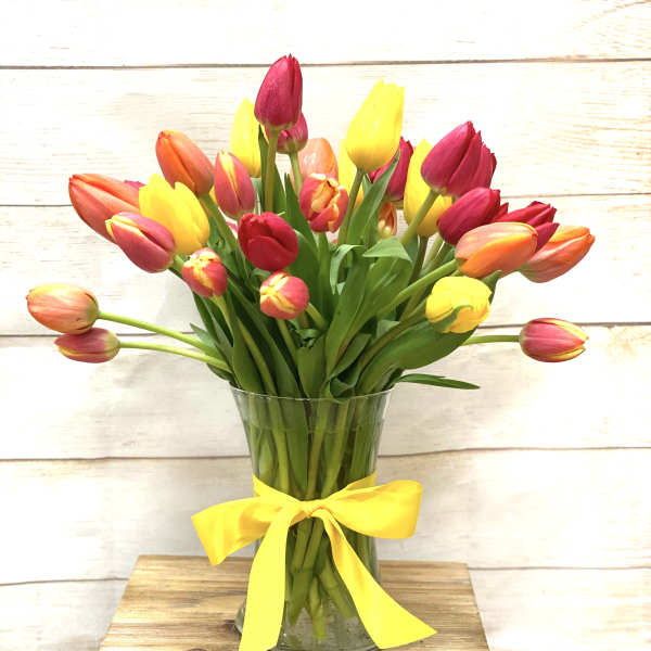 Mixed red, yellow, and orange tulips in a clear glass vase with a yellow ribbon bow.