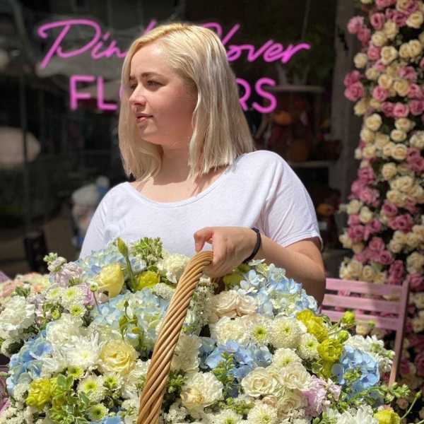 Woman holding a large basket of pastel flowers outside a flower shop