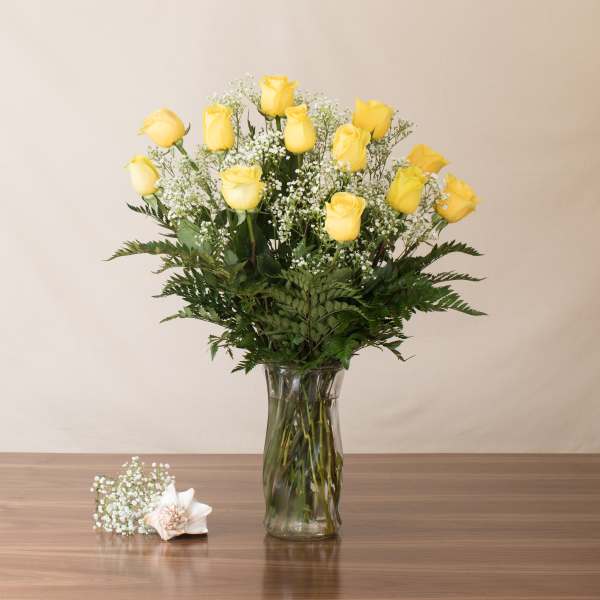 Tall arrangement of yellow roses with white accent flowers in a clear glass vase