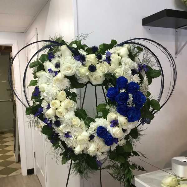 Heart-shaped floral wreath with white and blue roses on a stand