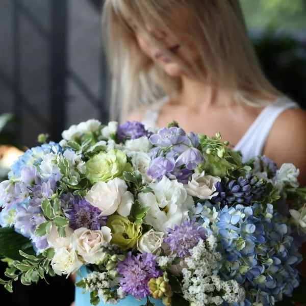 Woman holding a large bouquet of blue, purple, and white flowers in a blue box