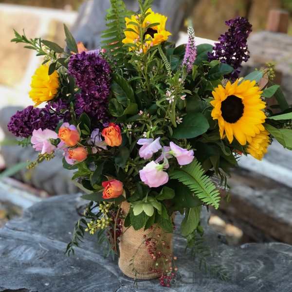 Bouquet with sunflowers, purple lilacs, and pink roses in a burlap-wrapped vase