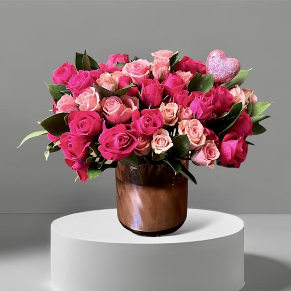 Pink and blush roses arranged in a brown glass vase with a glitter heart pick