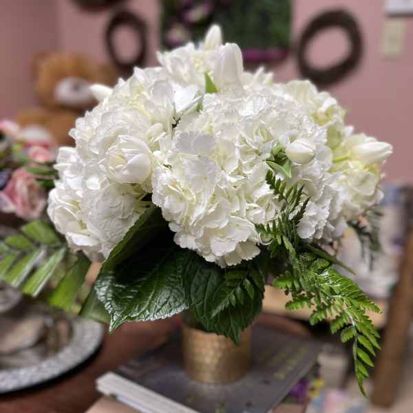White floral arrangement in a gold vase with green foliage