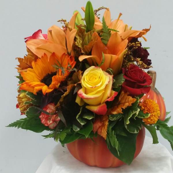 Autumn bouquet in a pumpkin-shaped vase with sunflowers, roses, and lilies