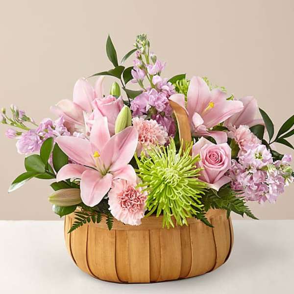 Pink lilies and roses arranged in a wooden basket