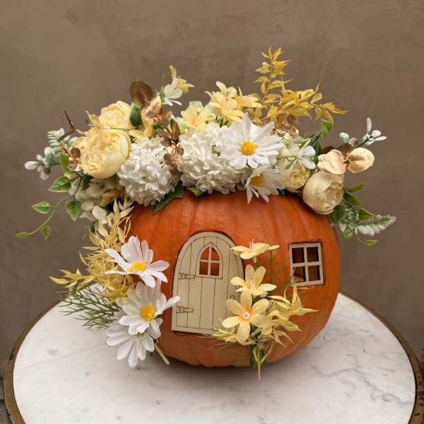 Pumpkin decorated with white and yellow flowers and a small door cutout