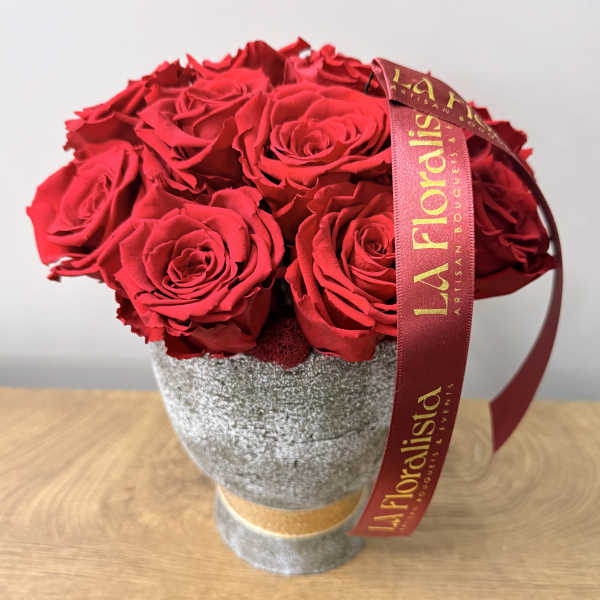 Red roses arranged in a gray textured vase with a burgundy ribbon