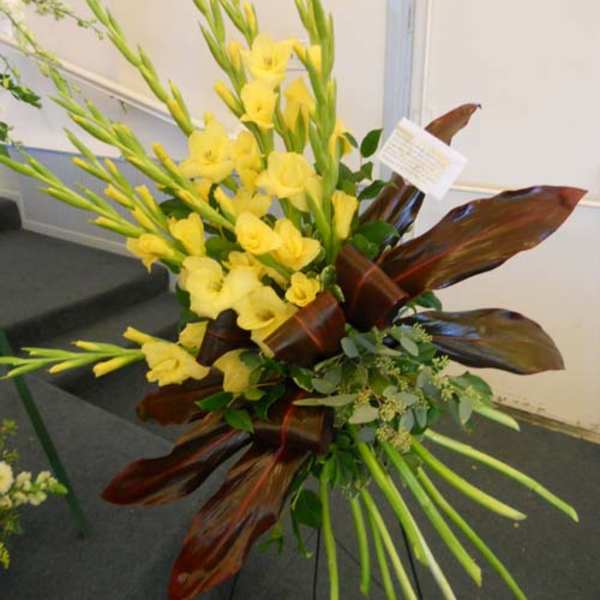 Tall yellow floral arrangement with long stems and dark red leaves