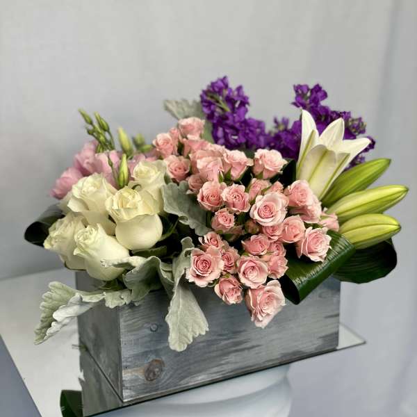Bouquet of pink and white roses with purple flowers in a wooden box