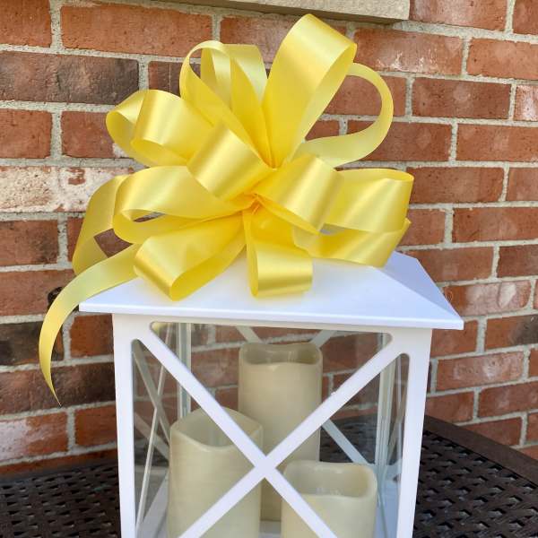 White lantern with three candles and a large yellow bow on top