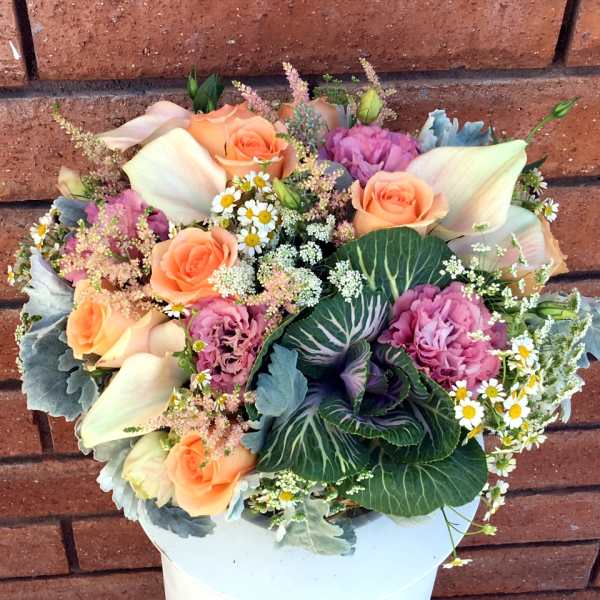Bouquet of peach roses, pink blooms, and white calla lilies in a white container