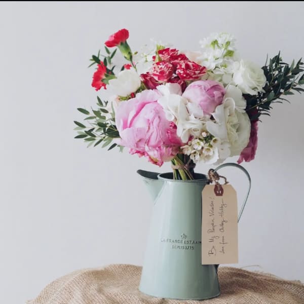Pink and white flower bouquet in a pale blue metal pitcher