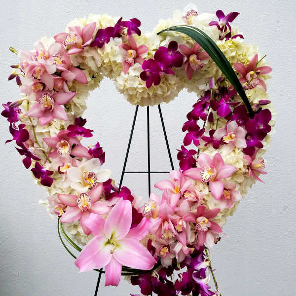 Heart-shaped floral wreath with pink and purple orchids on a stand