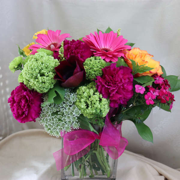 Bright mixed bouquet in a clear glass vase with a pink ribbon