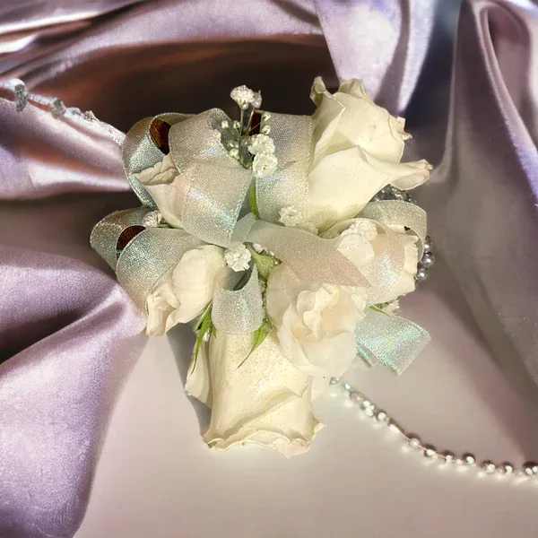 Small white rose corsage with silver ribbon on satin fabric