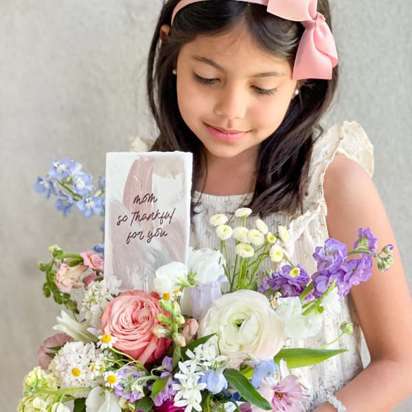 Girl holding a pastel mixed flower arrangement with a thank-you card