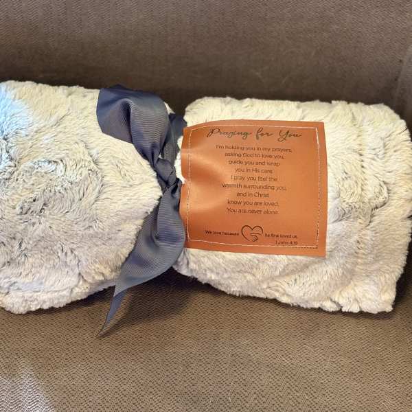 Two folded plush blankets tied with a ribbon and prayer tag