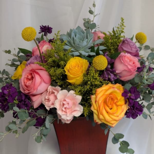 Mixed arrangement of pink and yellow roses, purple flowers, and a succulent in a red-brown vase