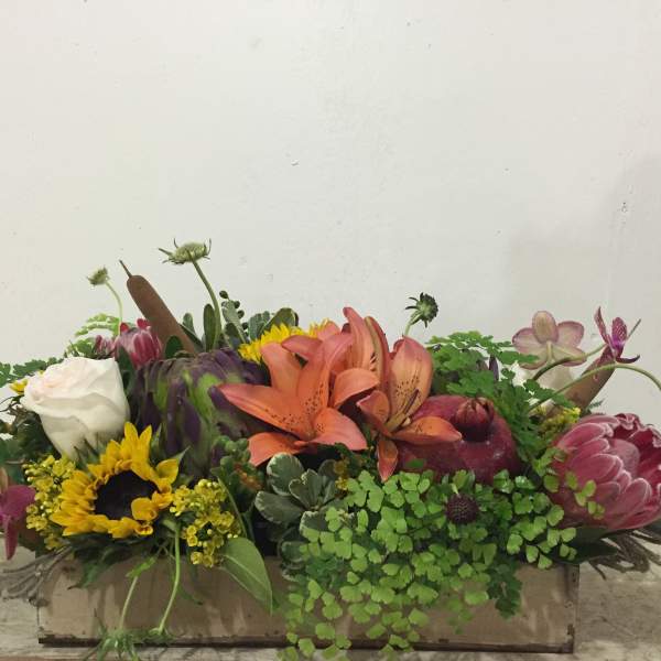 Mixed floral arrangement with lilies, sunflowers, roses, and protea in a low container