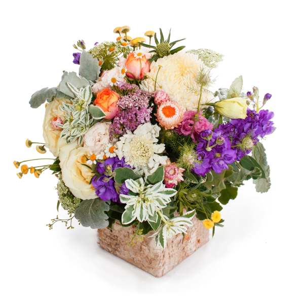 Mixed bouquet in a square bark-covered vase with cream, purple, and peach flowers