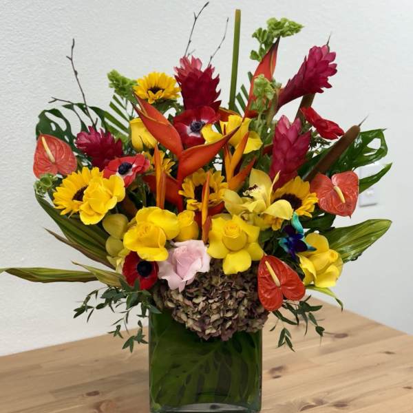 Tropical bouquet with yellow sunflowers and red-orange blooms in a green vase