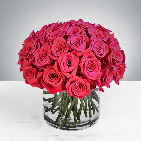 A round bouquet of bright pink roses in a clear glass vase.